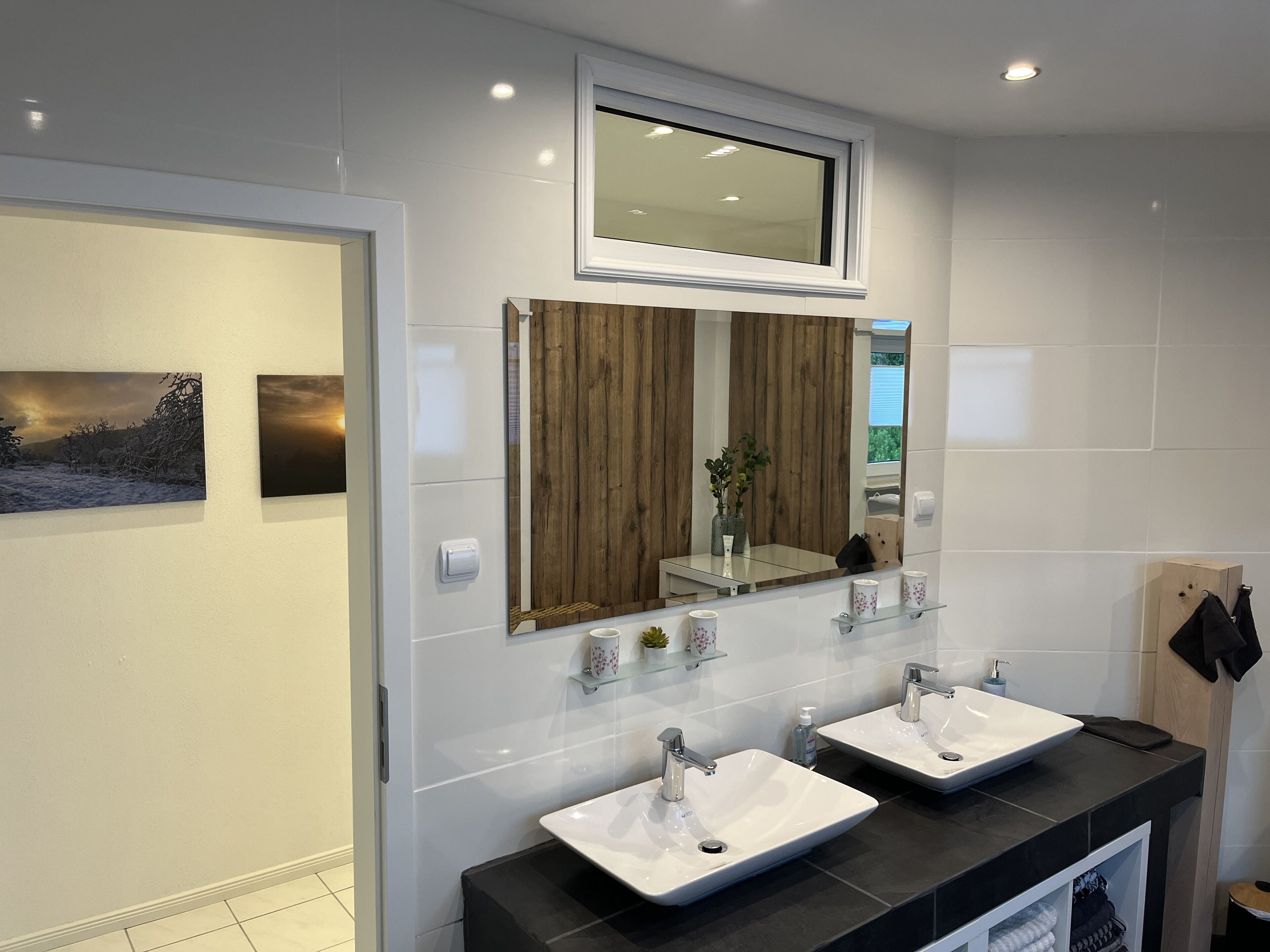 A modern bathroom with two white sinks, a large mirror, and a wooden panel accent.