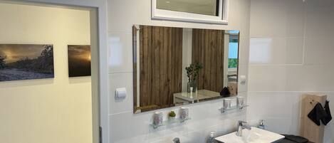 A modern bathroom with two white sinks, a large mirror, and a wooden panel accent.