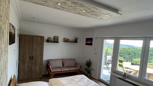 A bedroom with two beds, a wooden wardrobe, a striped sofa, and a view of a mountainous landscape through large windows.