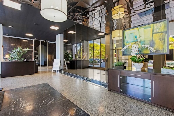 A modern lobby with a reception desk, large windows, and indoor plants.