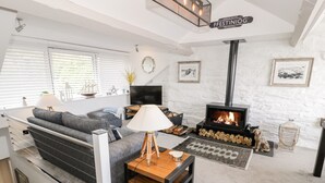 A cozy living room with a sofa, a table, a TV, a fireplace, and a sign reading "FFESTINIOG". - The Sail Loft (Porthmadog)