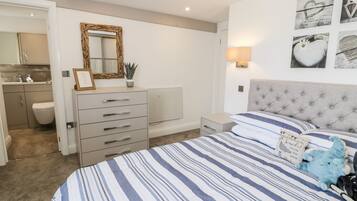 A bedroom with a large bed, a dresser, a nightstand, a mirror, and a wall with framed pictures.