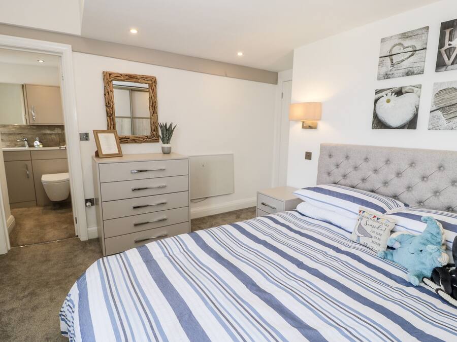 A bedroom with a large bed, a dresser, a nightstand, a mirror, and a wall with framed pictures.