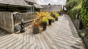 A wooden deck with potted plants, a wooden fence, and a stone wall. - The Sail Loft (Porthmadog)