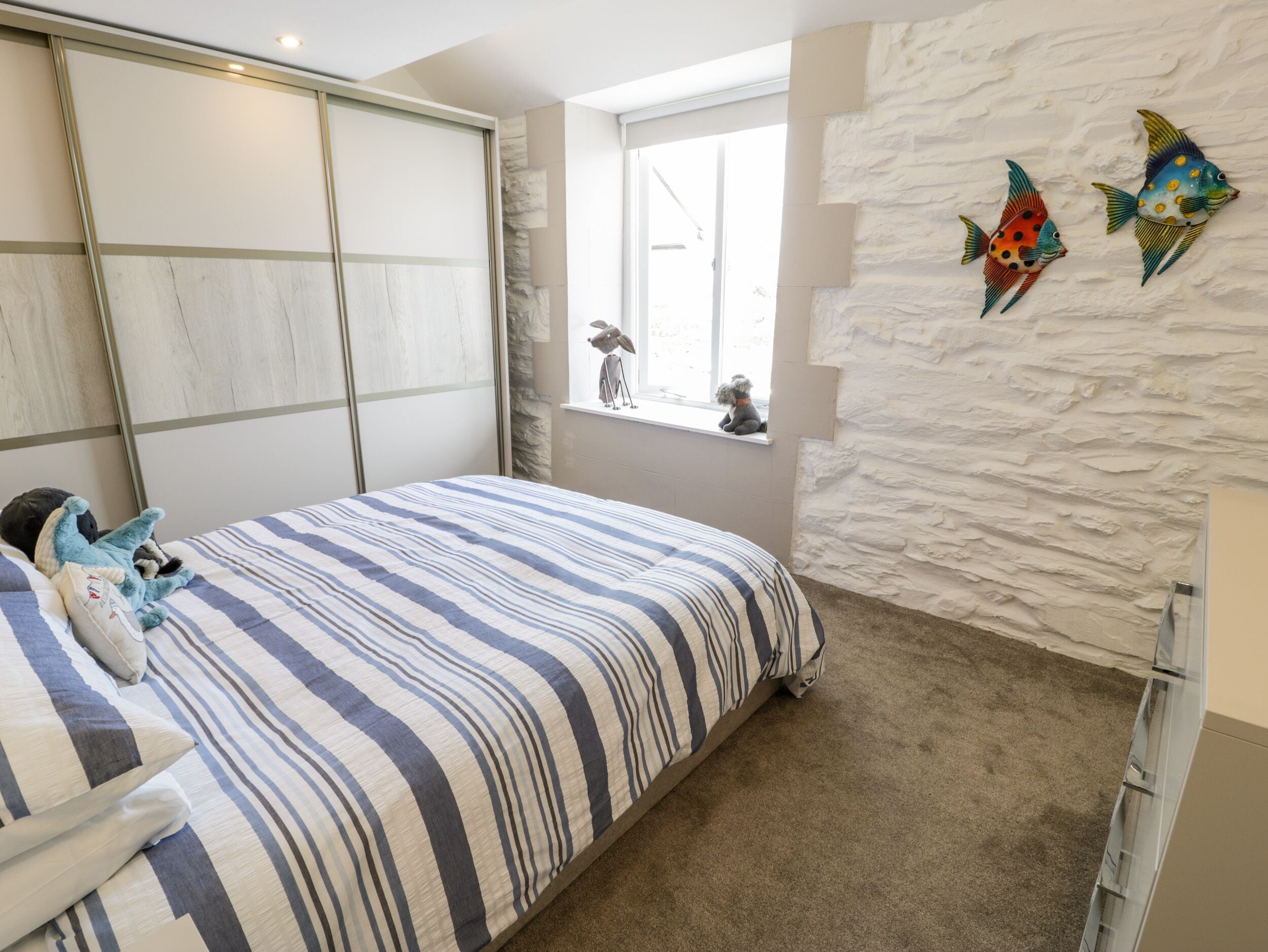 A bedroom with a striped bedspread, a window with a view, and decorative fish wall art.