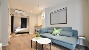 A modern living room with a sofa, a small coffee table, and a TV mounted on the wall. - Real Life Meguro River Superb 2BR 6pax Shibuya (Tokyo)