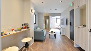 A modern hotel room with a kitchenette, a seating area with a sofa and a small table, and a television mounted on the wall. - Real Life Meguro River Superb 2BR 6pax Shibuya (Tokyo)