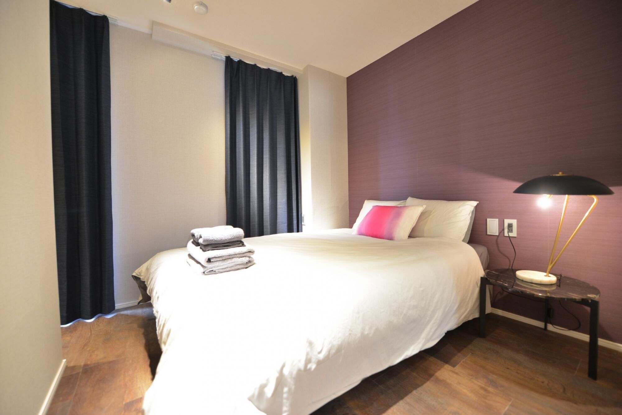 A bedroom with a bed, a nightstand, a lamp, and a window with curtains.