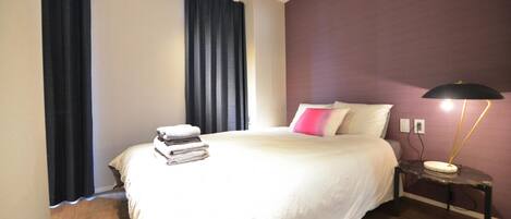 A bedroom with a bed, a nightstand, a lamp, and a window with curtains.