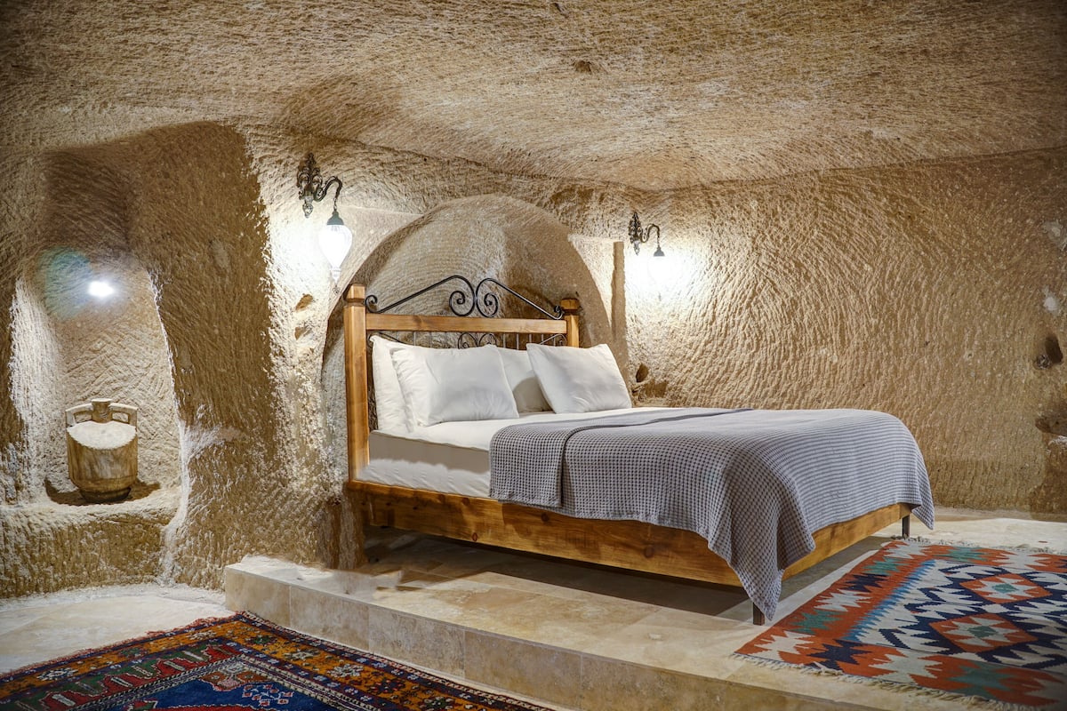 Un dormitorio con cama de madera, ropa de cama blanca y alfombra estampada.