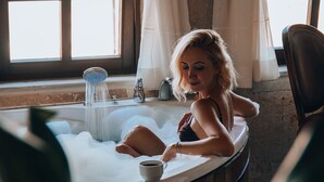 A person relaxing in a bathtub with a window and curtains in the background. - Karma Cappadocia (Nevsehir)