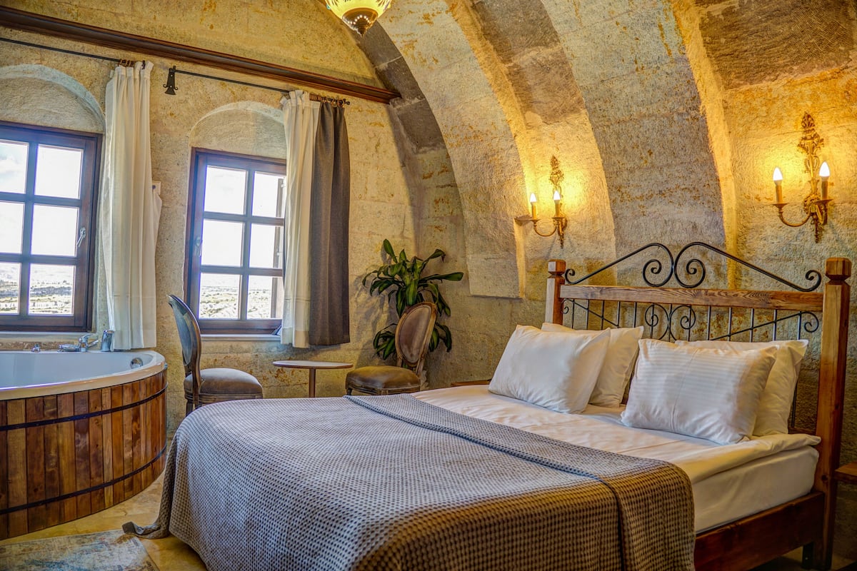 Un dormitorio con cama de madera, una bañera y vista al mar a través de una ventana.