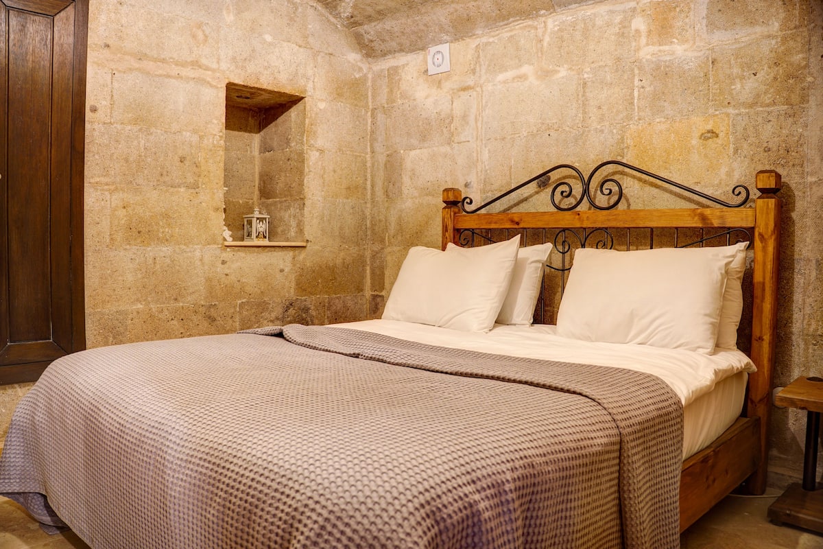 Un dormitorio con pared de piedra, estructura de cama de madera y una mesita de noche pequeña.