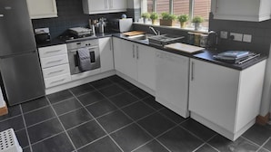 A modern kitchen with white cabinets, a black tiled backsplash, and a window overlooking a garden. - Castleview Large 3 Bedroom Family House - Glenarm (Ballymena)