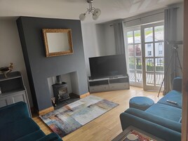Una sala de estar con chimenea, televisor, sofá y un ventanal con vistas a edificios y zonas verdes.
