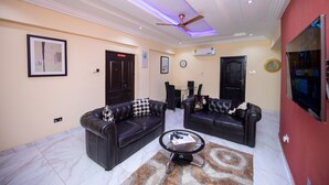 A living room with two black leather sofas, a glass coffee table, and a ceiling fan. - Executive One Bedroom Furnished Apartment in Accra (Accra)