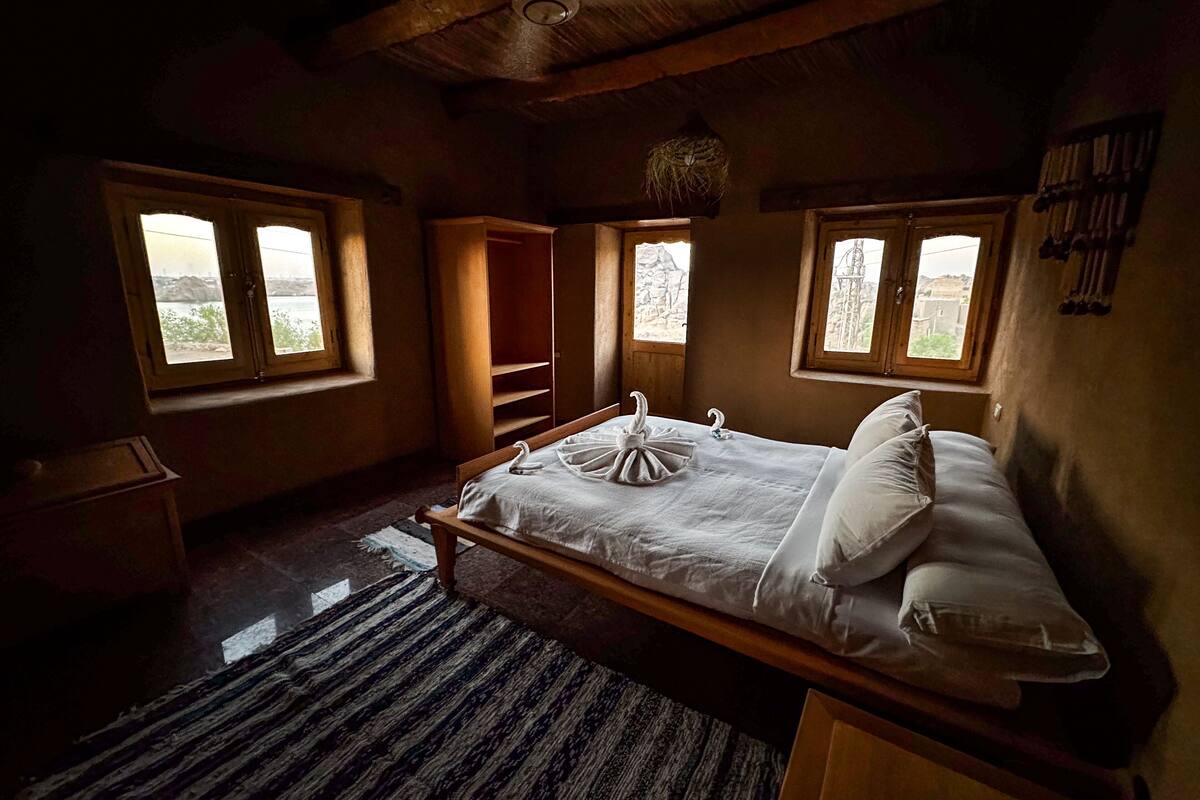 A bedroom with a wooden bed, two windows, a wardrobe, and a hanging light fixture.