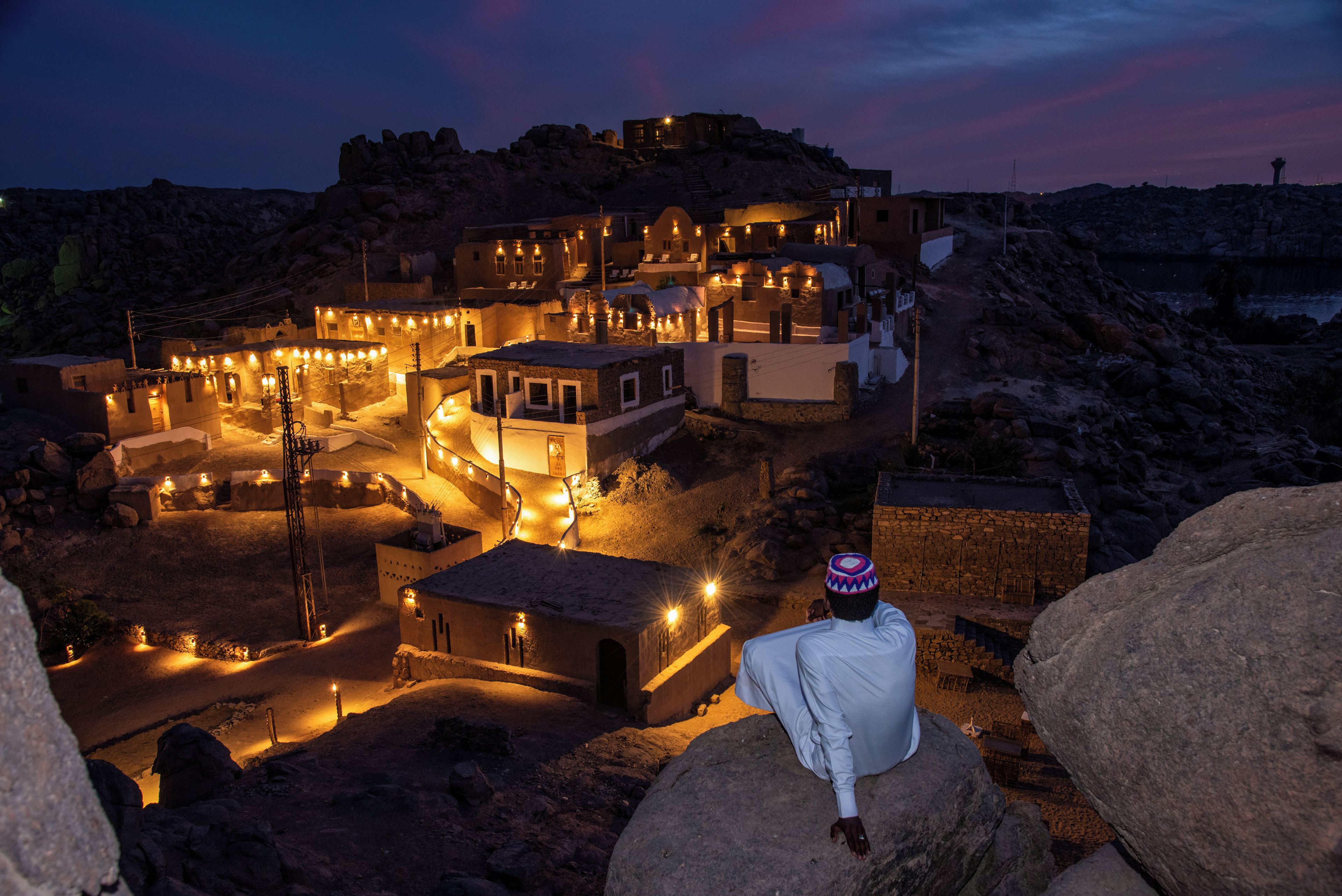 A traditional village at dusk with stone buildings and a person sitting on a rock.