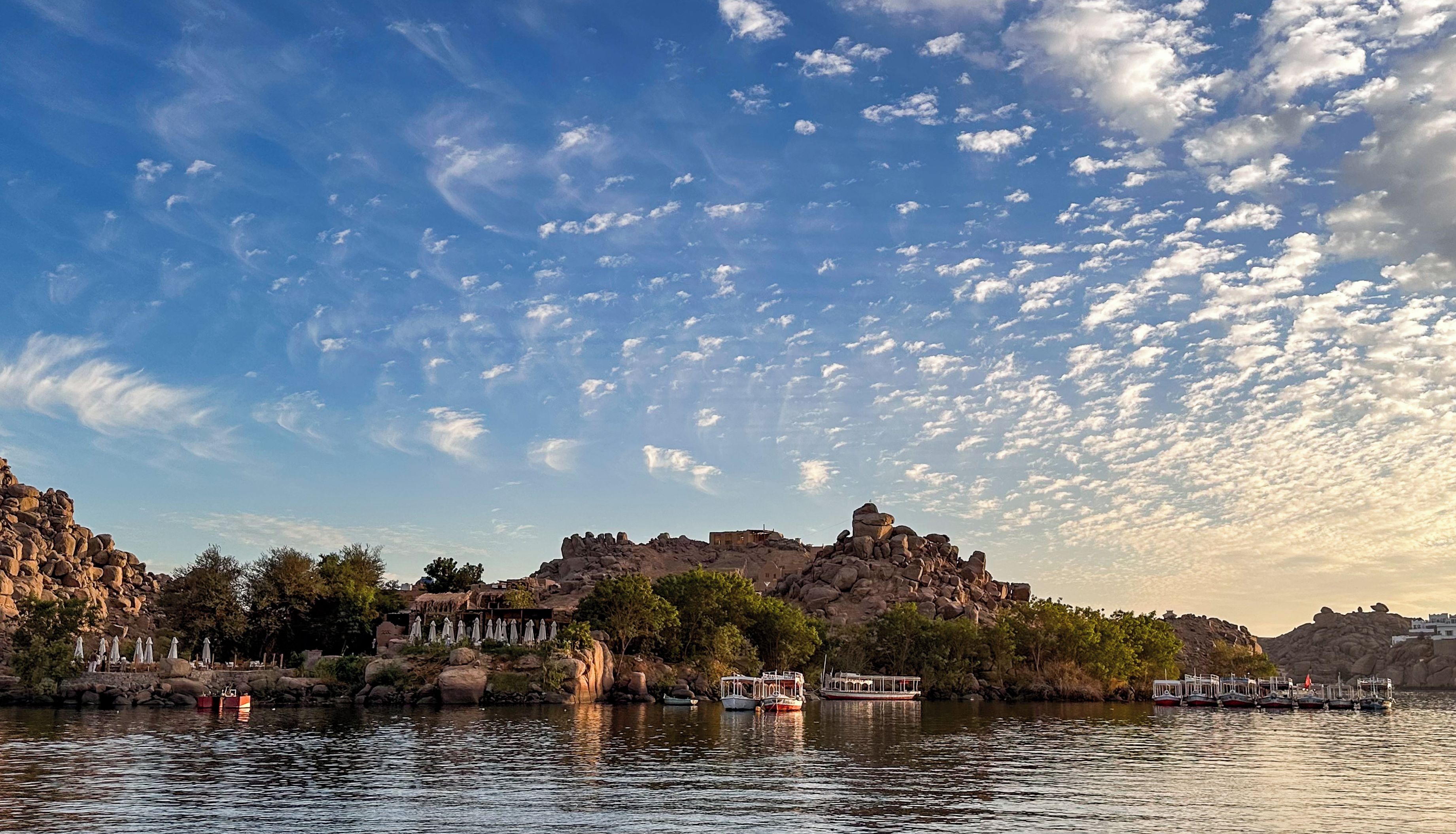 A rocky shoreline with boats docked, a clear sky, and a small building on the rocks.