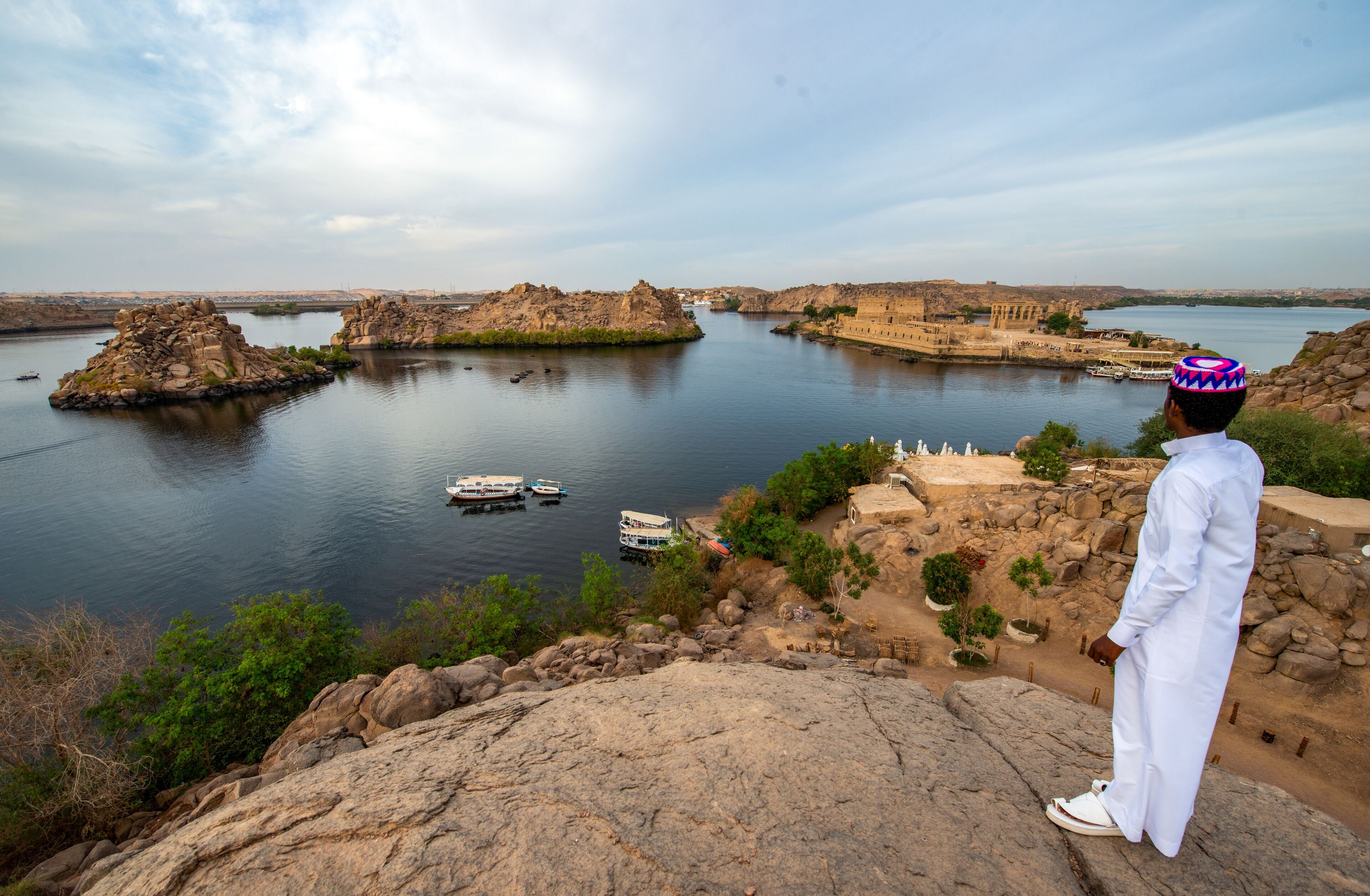 A man in traditional attire overlooking a river with boats and historical structures.