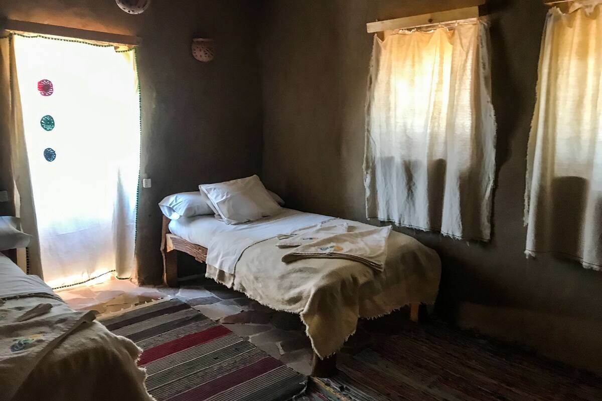 A small, dimly lit room with a single bed, a wooden floor, and a window with curtains.