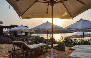 Relax on a line of sun loungers paired with white cushions under large umbrellas on the sandy beach.