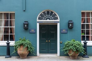 A building facade with a dark blue exterior, a symmetrical entrance with double doors, and two potted plants on either side.