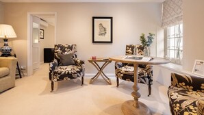 Una sala de estar con dos sillones estampados, una mesa redonda de madera y una obra de arte enmarcada en la pared.