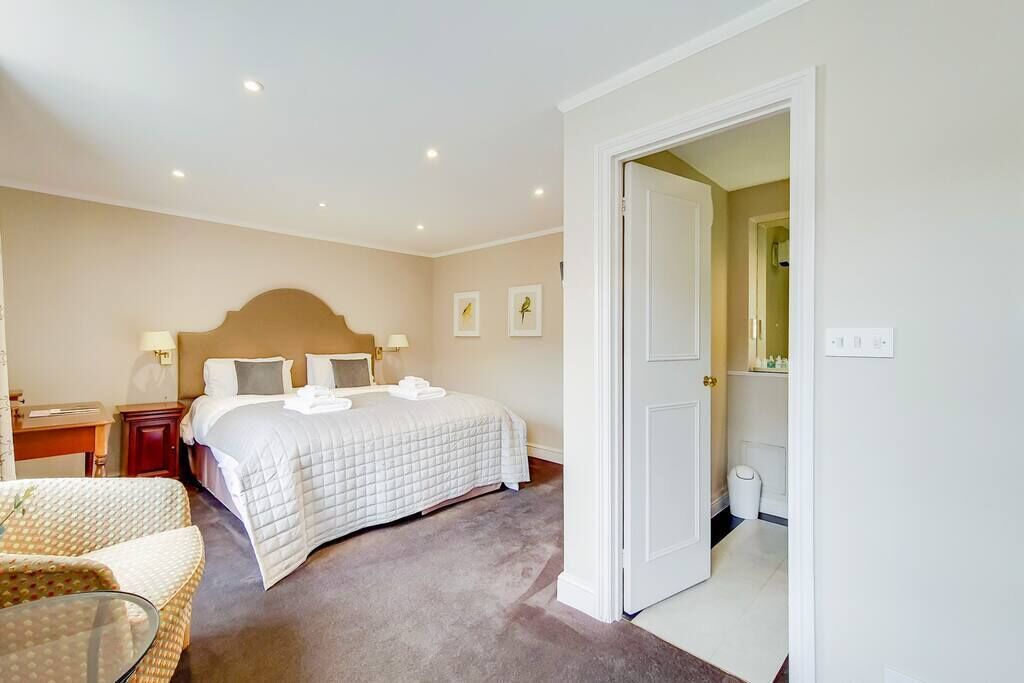 A hotel room with a bed, bedside tables, a chair, and a bathroom visible through an open door.
