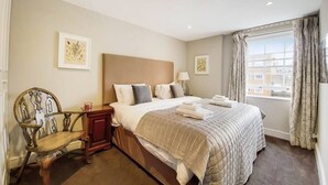 Une chambre d’hôtel avec un grand lit, une chaise en bois, une table de chevet et une fenêtre avec des rideaux.