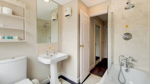 Une salle de bain équipée de toilettes, d’un lavabo, d’un miroir, d’une douche et d’étagères contenant des articles de toilette.