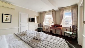Quarto de hotel com uma cama grande, uma escrivaninha, uma cadeira, uma televisão e uma janela com cortinas.