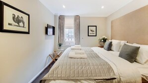 Quarto de hotel com cama grande, televisão de tela plana, janela com cortinas e obras de arte nas paredes.