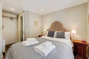 A neatly made bed with two folded white towels, a bedside table with a lamp, and a door to the left.