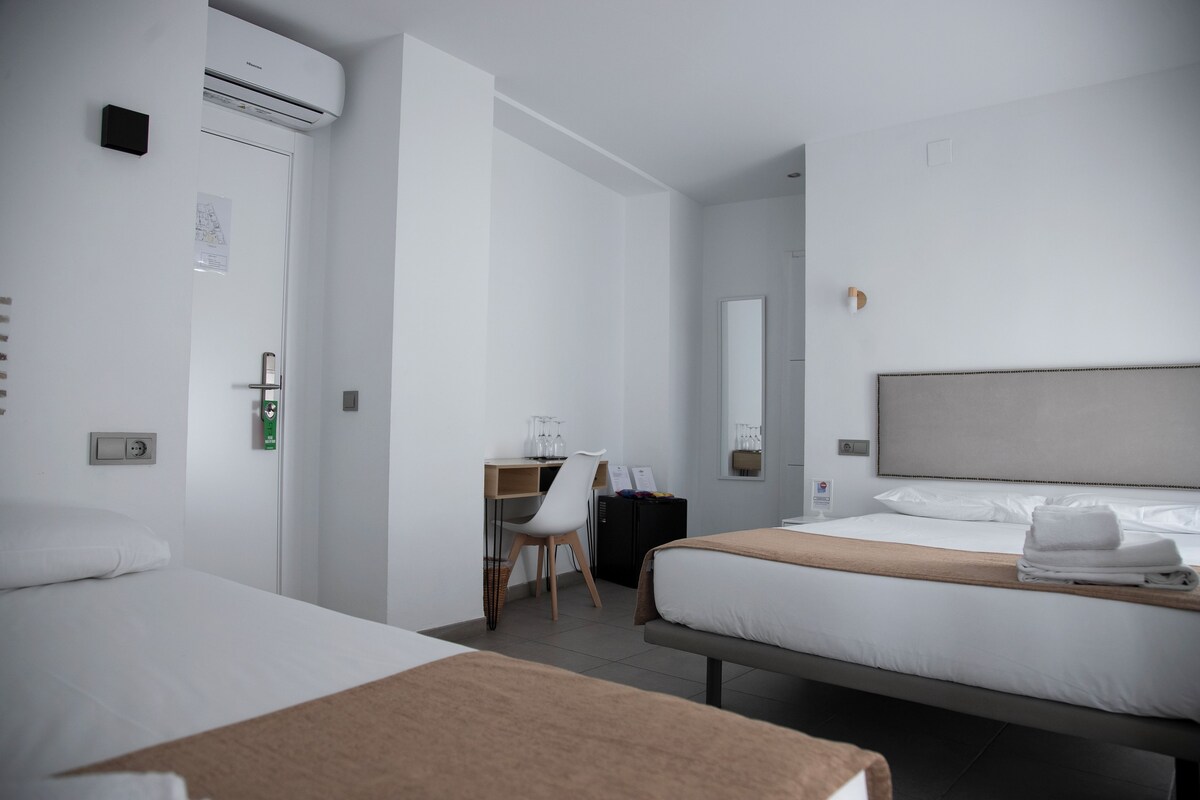 Una habitación de hotel con dos camas, un escritorio, una silla y un espejo grande.