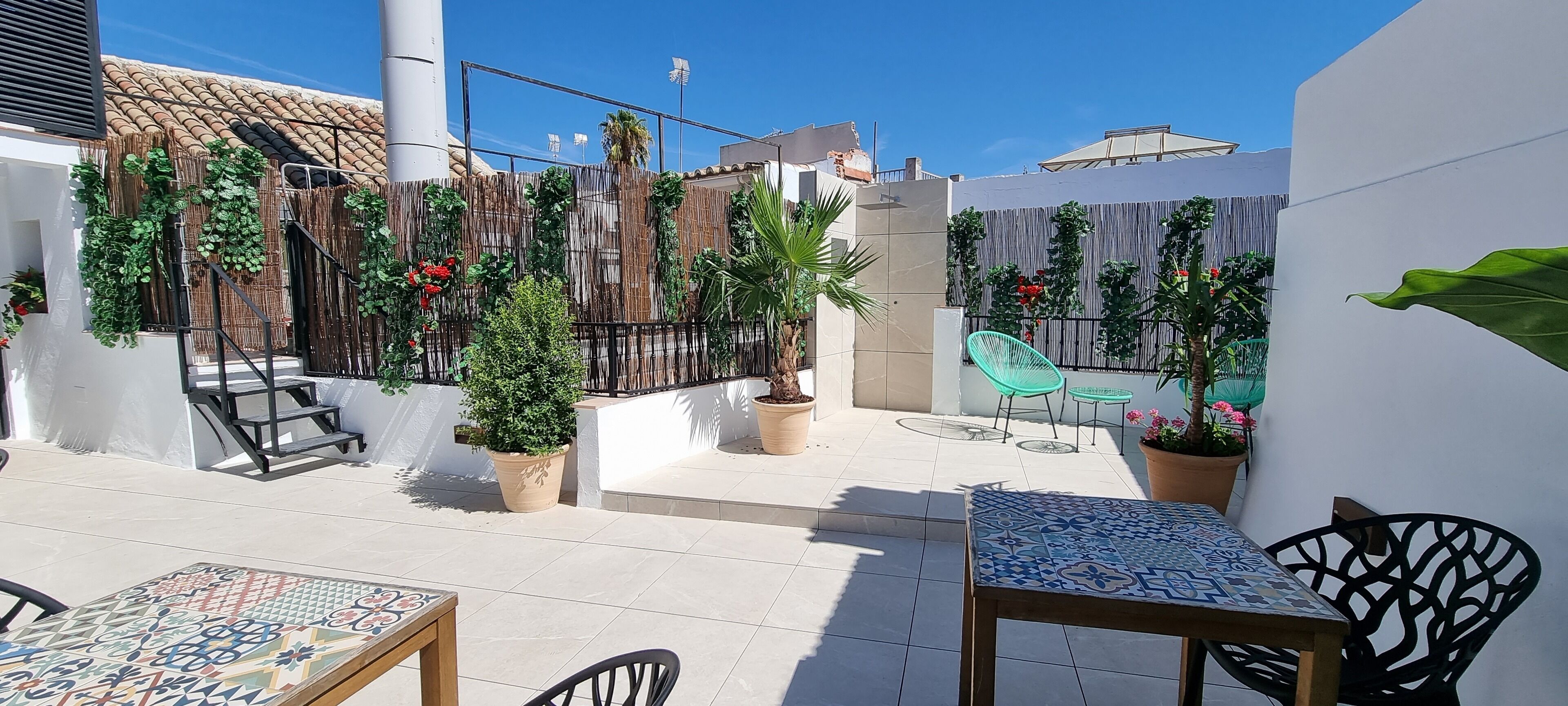 A patio area with tiled flooring, outdoor furniture, potted plants, and a bamboo fence.