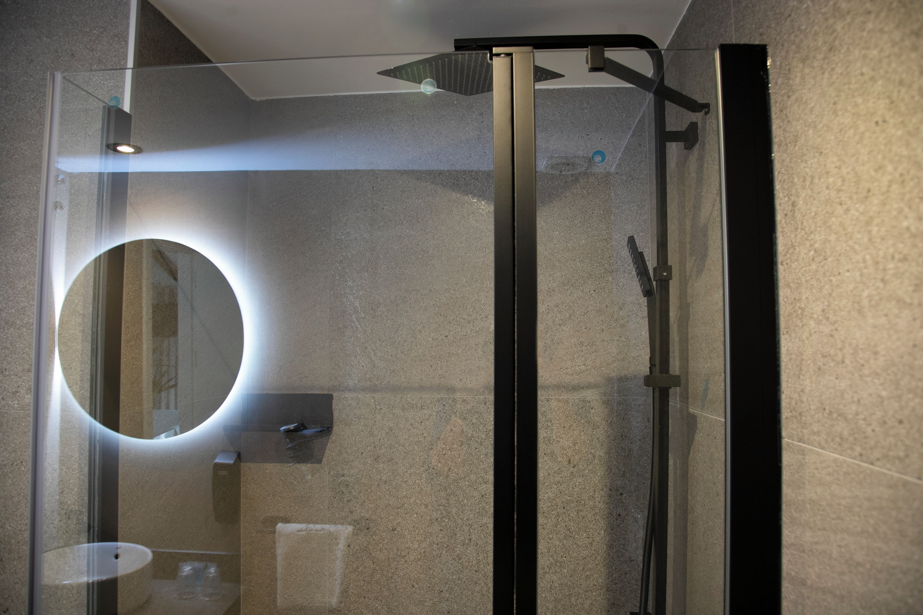 A modern bathroom with a glass-enclosed shower, a round mirror, and a visible towel rack.