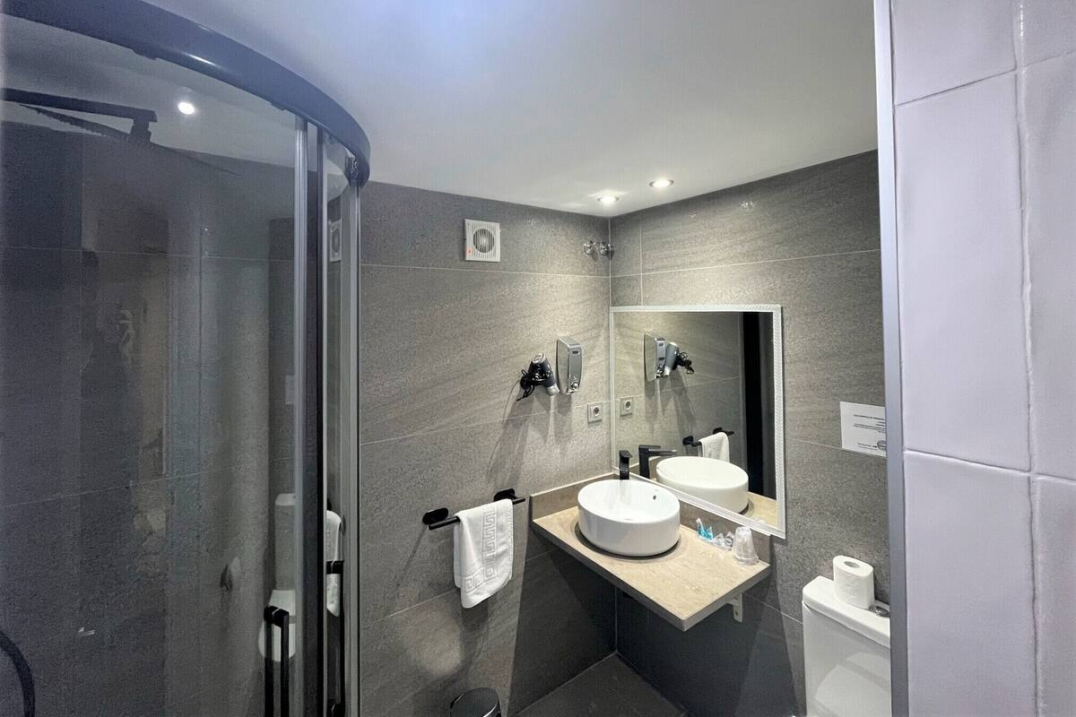 Een moderne badkamer met een douchecabine van glas, een wastafel met twee kommen en een toilet.