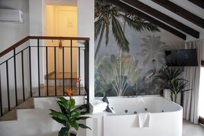 A modern bathroom with a large bathtub, a staircase with a wooden railing, and a tropical mural on the wall. - Vitium Cordoba (Córdoba)