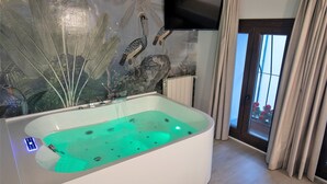 A modern bathroom with a large bathtub, a wall-mounted TV, and a view through a glass door. - Vitium Cordoba (Córdoba)