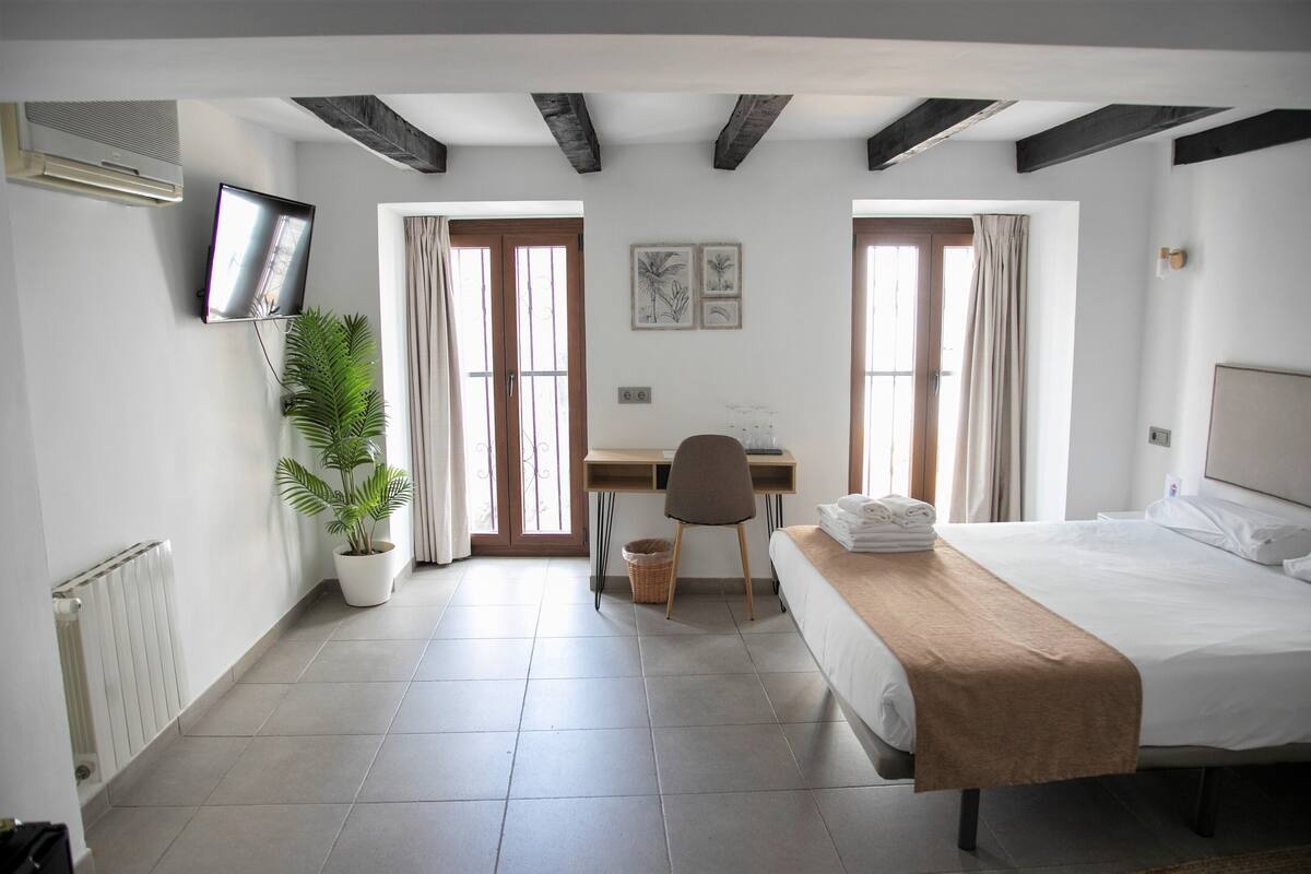 Een hotelkamer met een bed, bureau, stoel, kamerplant en een televisie.