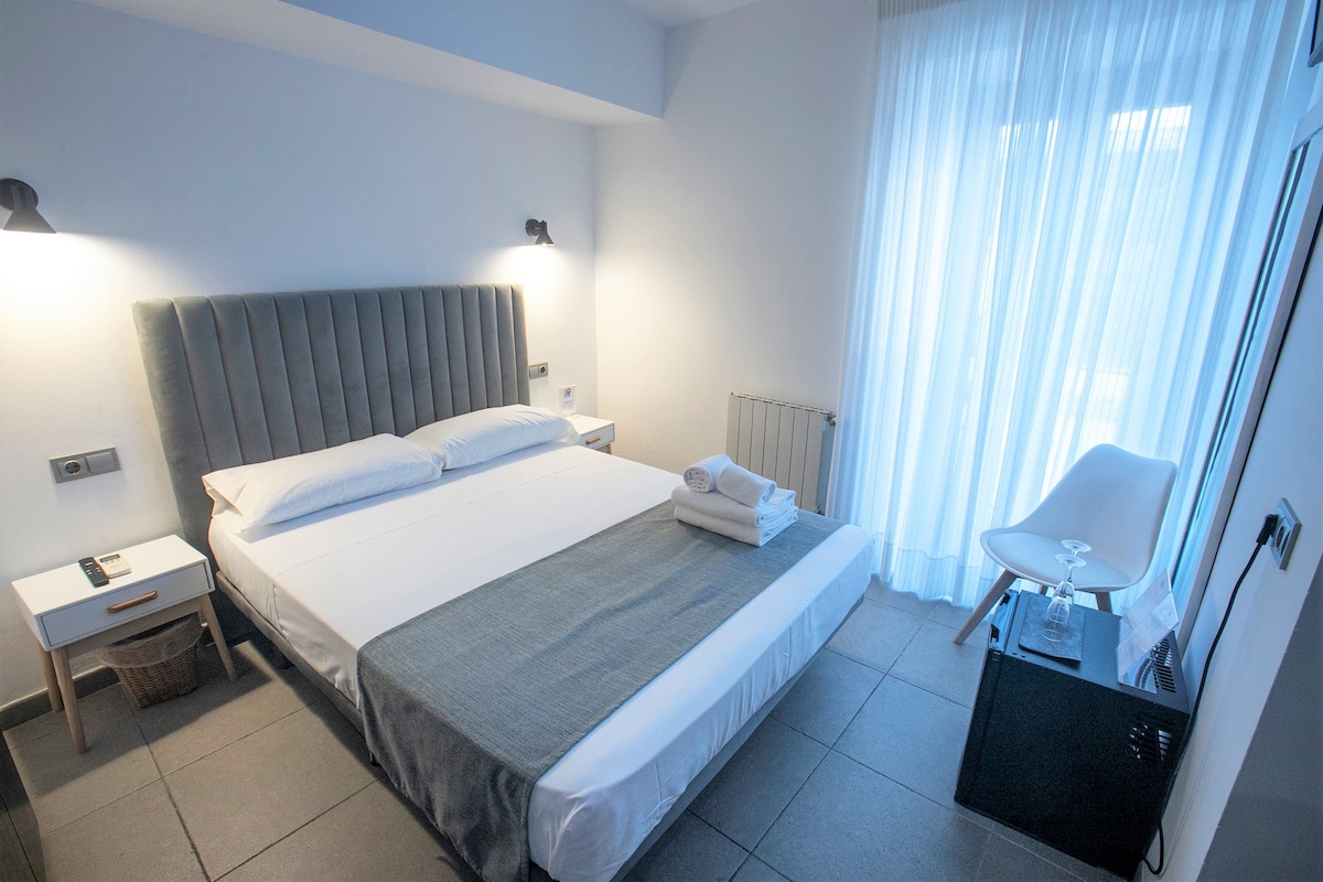 Una habitación de hotel con cama, mesitas de noche, una silla y un radiador.