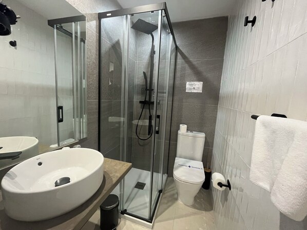 Un baño moderno con cabina de ducha de vidrio, inodoro y dos lavamanos.