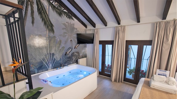 A modern bathroom with a large bathtub, a wall-mounted TV, and a view of the outdoors through a glass door. - Vitium Cordoba (Córdoba)