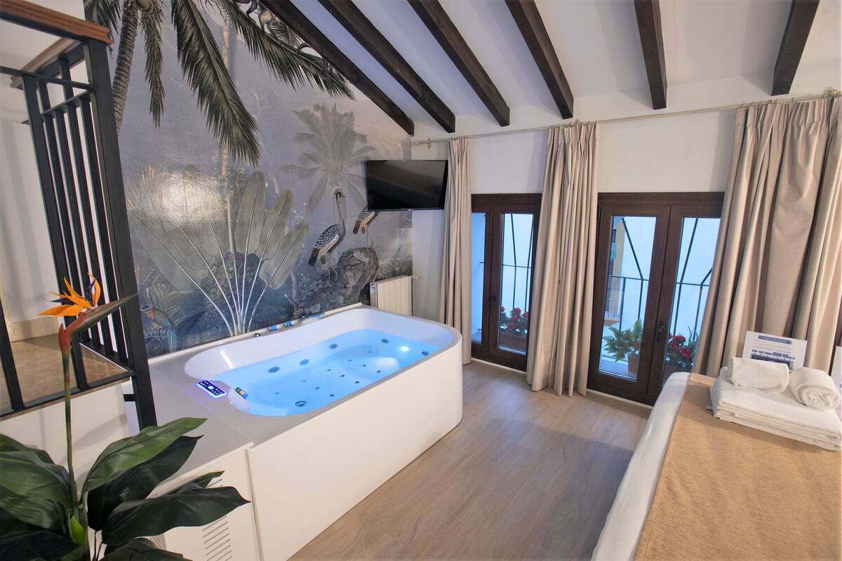 Een moderne badkamer met een groot bad, een televisie aan de muur en uitzicht op het groen door een glazen deur.