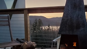 A wood-burning stove on a deck with a view of a lake and mountains in the background. - Eagles Nest Converted Shipping Container at Sally's Brook Wilderness Cabins (Englishtown)