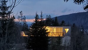 A modern cabin with a glass facade, surrounded by trees and a mountain in the background. - Eagles Nest Converted Shipping Container at Sally's Brook Wilderness Cabins (Englishtown)