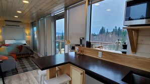 A modern kitchen with a wooden ceiling, a large window, and a television. - Eagles Nest Converted Shipping Container at Sally's Brook Wilderness Cabins (Englishtown)