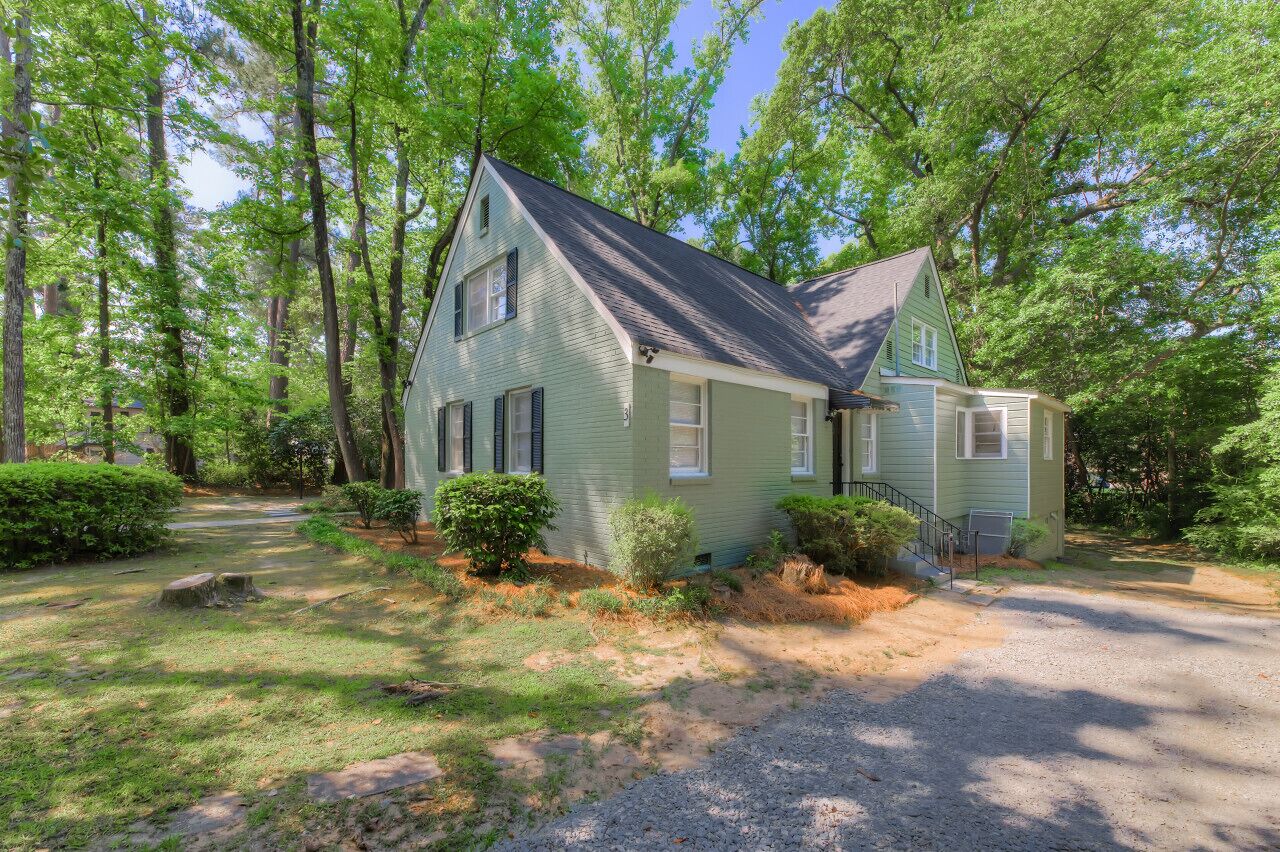 A two-story house with a sloped roof, surrounded by a wooded area.