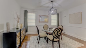 Uma sala de jantar com mesa de vidro, quatro cadeiras, um aparador preto e um lustre.